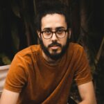 Portrait of a stylish man with glasses and beard sitting casually outdoors.